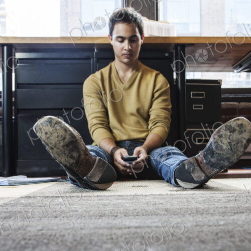 Hispanic man on his cell phone while sitting on floor at his office workstation. Hispanic man on his cell phone while sitting on floor at his office workstation.