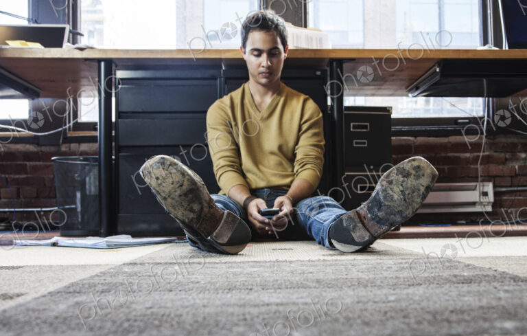 Hispanic man on his cell phone while sitting on floor at his office workstation.