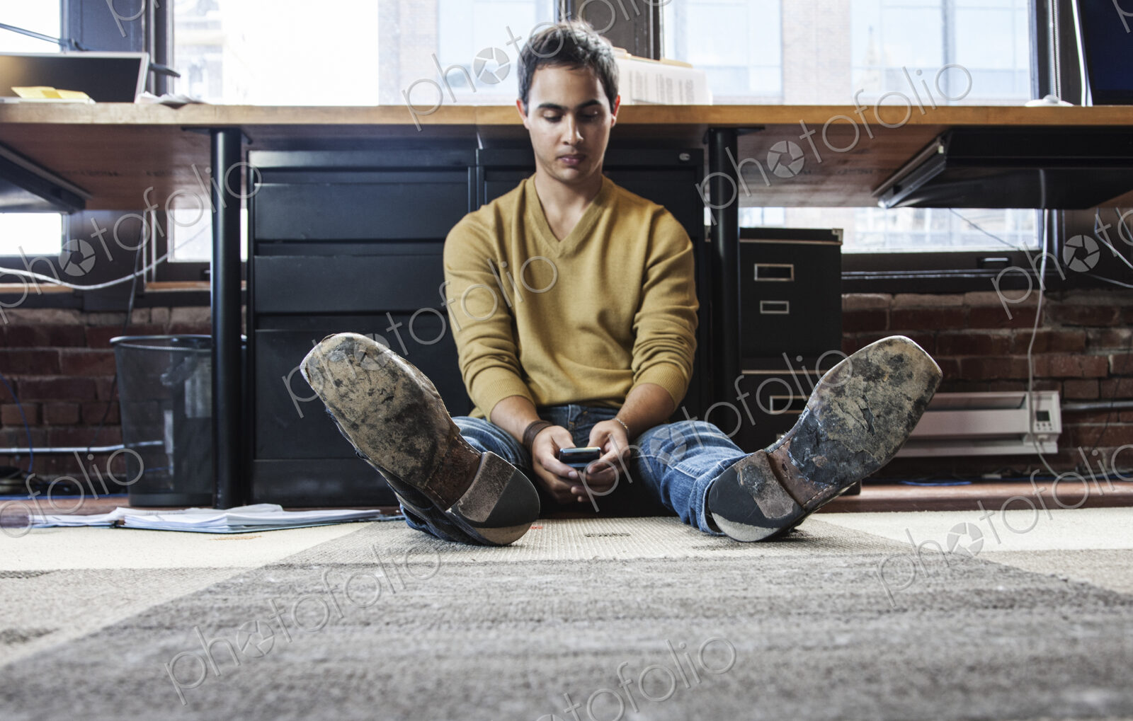 Hispanic man on his cell phone while sitting on floor at his office workstation.