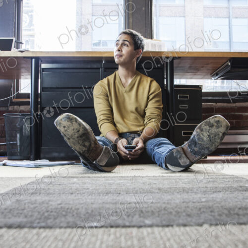 Hispanic man on his cell phone while sitting on floor at his office workstation. Hispanic man on his cell phone while sitting on floor at his office workstation.