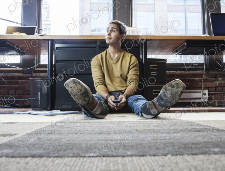 Hispanic man on his cell phone while sitting on floor at his office workstation.