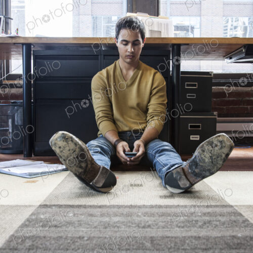 Hispanic man on his cell phone while sitting on floor at his office workstation. Hispanic man on his cell phone while sitting on floor at his office workstation.
