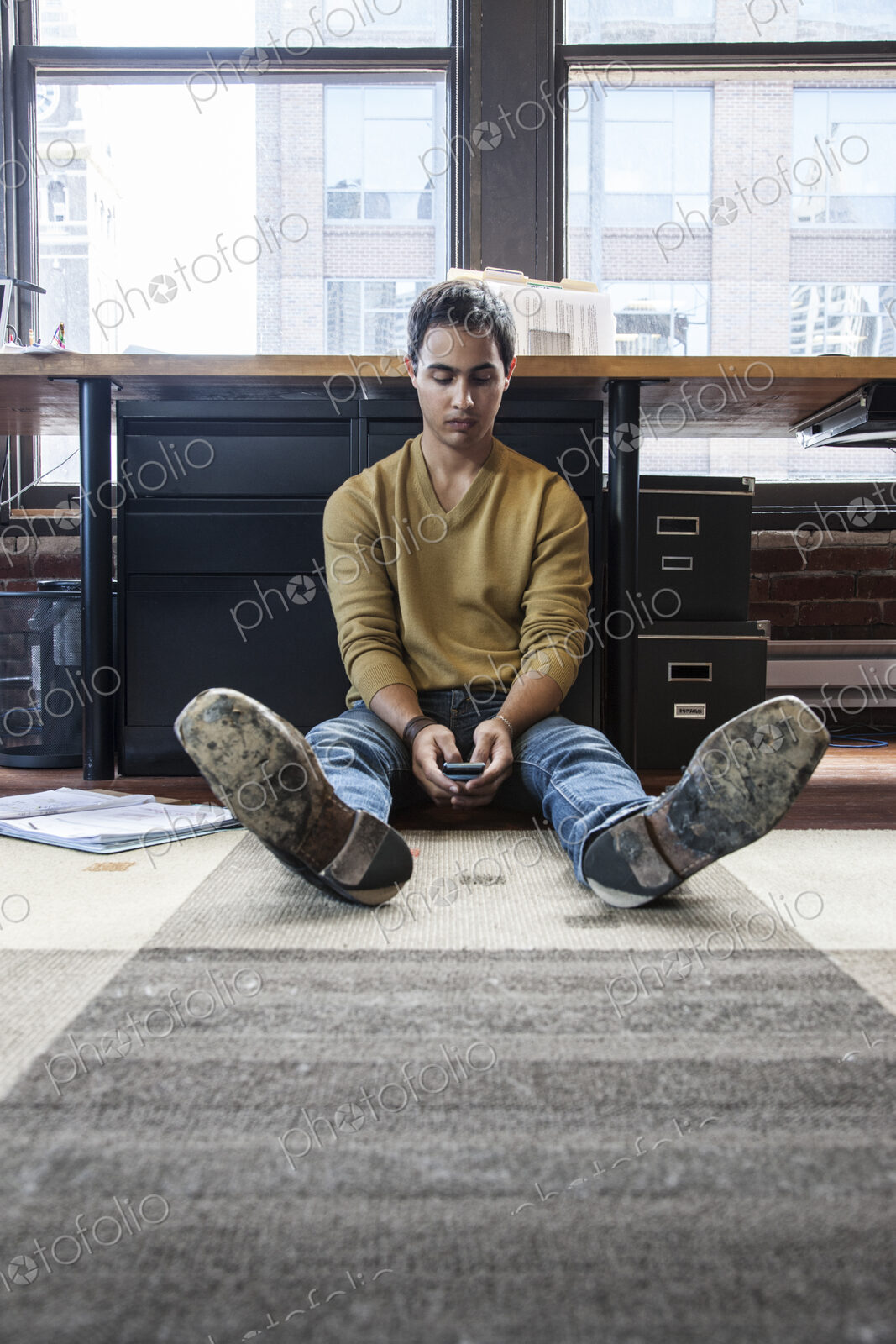 Hispanic man on his cell phone while sitting on floor at his office workstation.