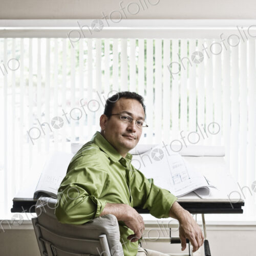 Hispanic man owner of a landscape company sitting at his design desk in the office.