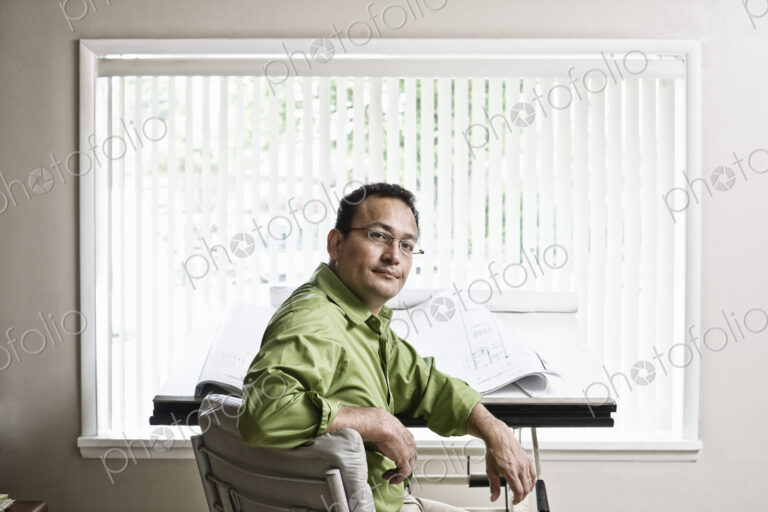 Hispanic man owner of a landscape company sitting at his design desk in the office.