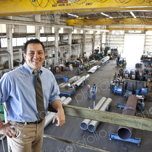 Hispanic man owner of a sheet metal factory stanidng above factory floor.