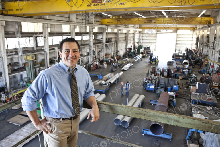 Hispanic man owner of a sheet metal factory stanidng above factory floor.