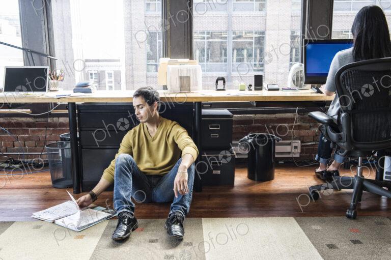 Hispanic man sitting on floor next to his work station in a creative office.