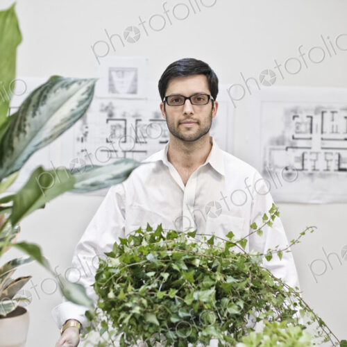 Hispanic man standing in an architect's office near large office plants. Hispanic man standing in an architect's office near large office plants.