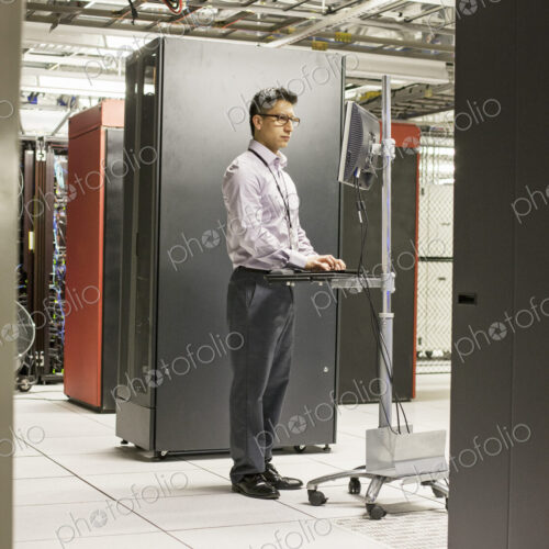 Hispanic man technician doing diagnostic tests on computer servers in a large server farm.