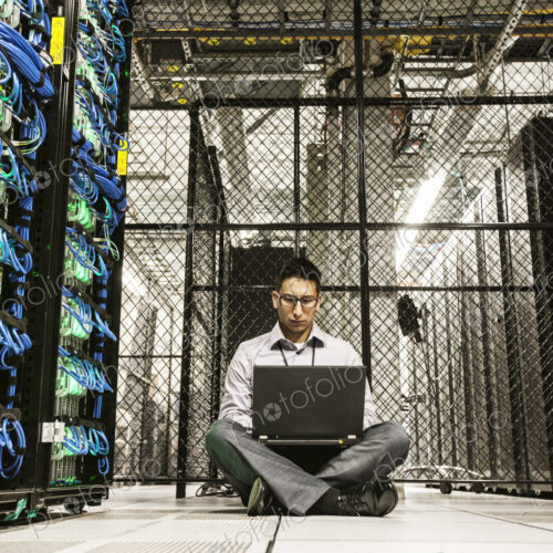 Hispanic man technician doing diagnostic tests on computer servers in a large server farm. Hispanic man technician doing diagnostic tests on computer servers in a large server farm.