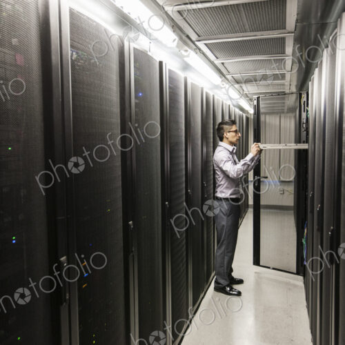 Hispanic man technician doing diagnostic tests on computer servers in a large server farm. Hispanic man technician doing diagnostic tests on computer servers in a large server farm.
