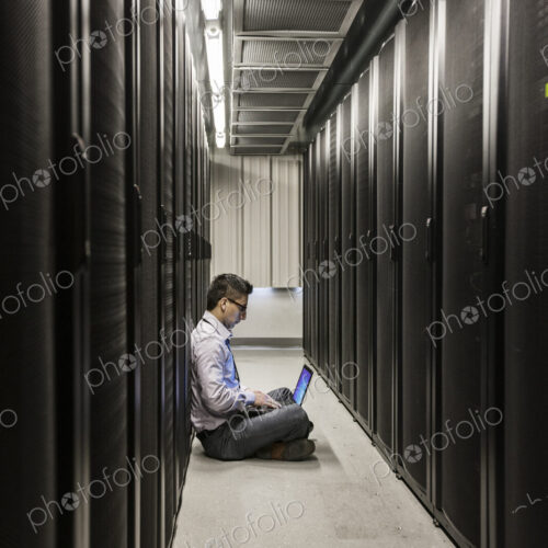 Hispanic man technician doing diagnostic tests on computer servers in a large server farm. Hispanic man technician doing diagnostic tests on computer servers in a large server farm.