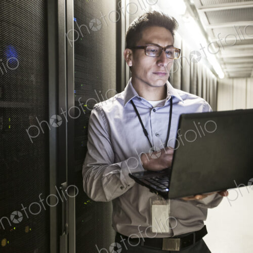 Hispanic man technician doing diagnostic tests on computer servers in a large server farm. Hispanic man technician doing diagnostic tests on computer servers in a large server farm.
