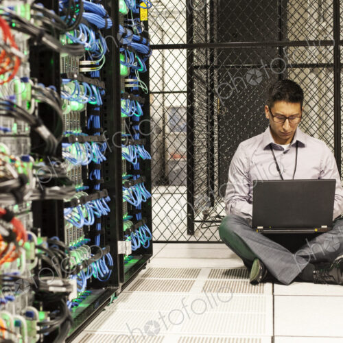 Hispanic man technician doing diagnostic tests on computer servers in a large server farm. Hispanic man technician doing diagnostic tests on computer servers in a large server farm.