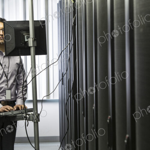 Hispanic man technician doing diagnostic tests on computer servers in a large server farm. Hispanic man technician doing diagnostic tests on computer servers in a large server farm.