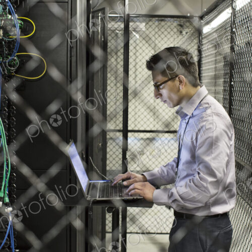 Hispanic man technician doing diagnostic tests on computer servers in a large server farm. Hispanic man technician doing diagnostic tests on computer servers in a large server farm.