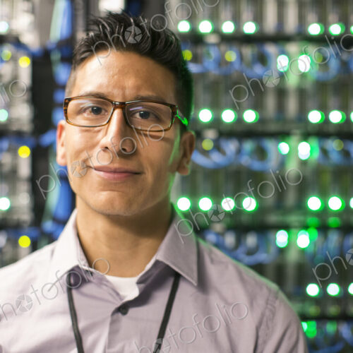 Hispanic man technician in a large computer server farm. Hispanic man technician in a large computer server farm.