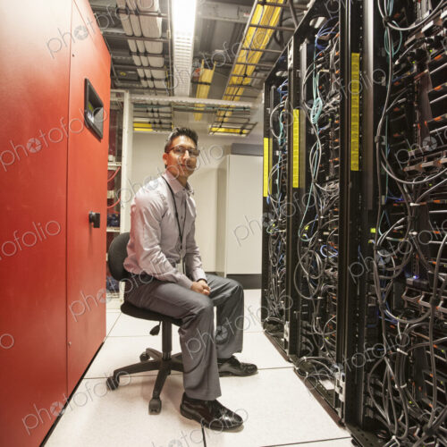 Hispanic man technician working with computer servers in a computer server farm. Hispanic man technician working with computer servers in a computer server farm.