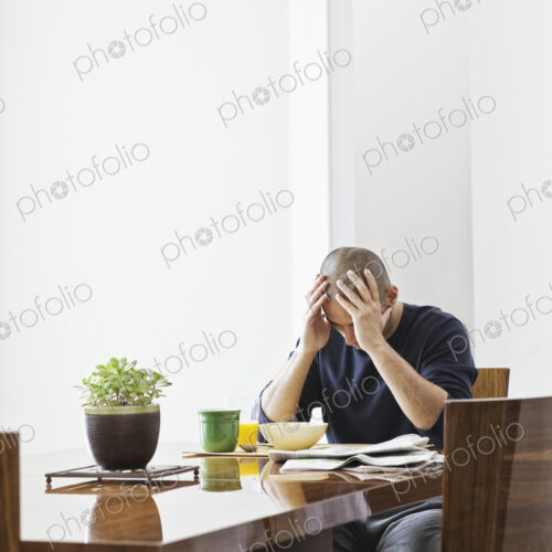 Hispanic man under stress while sitting at the dining room table in a new home. Hispanic man under stress while sitting at the dining room table in a new home.