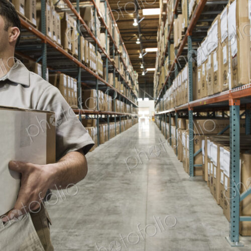 Hispanic warehouse worker carrying a box down an aisle in a large distrubiton warehouse. Hispanic warehouse worker carrying a box down an aisle in a large distrubiton warehouse.