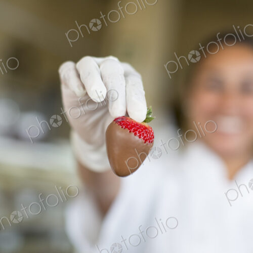 Hispanic woman holding a chocolate covered strawberry in a candy shop.
