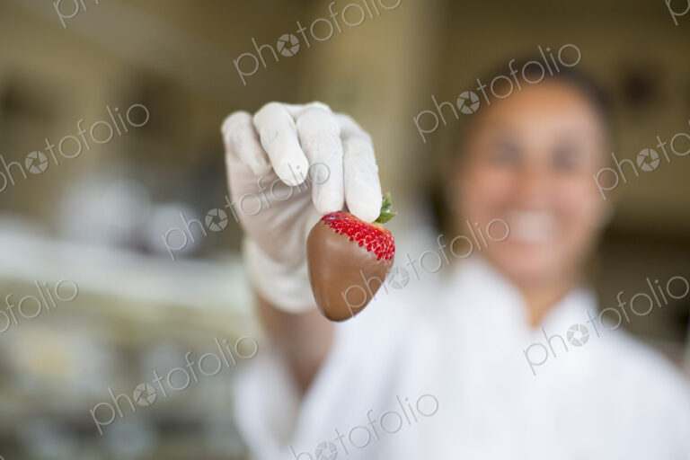 Hispanic woman holding a chocolate covered strawberry in a candy shop.
