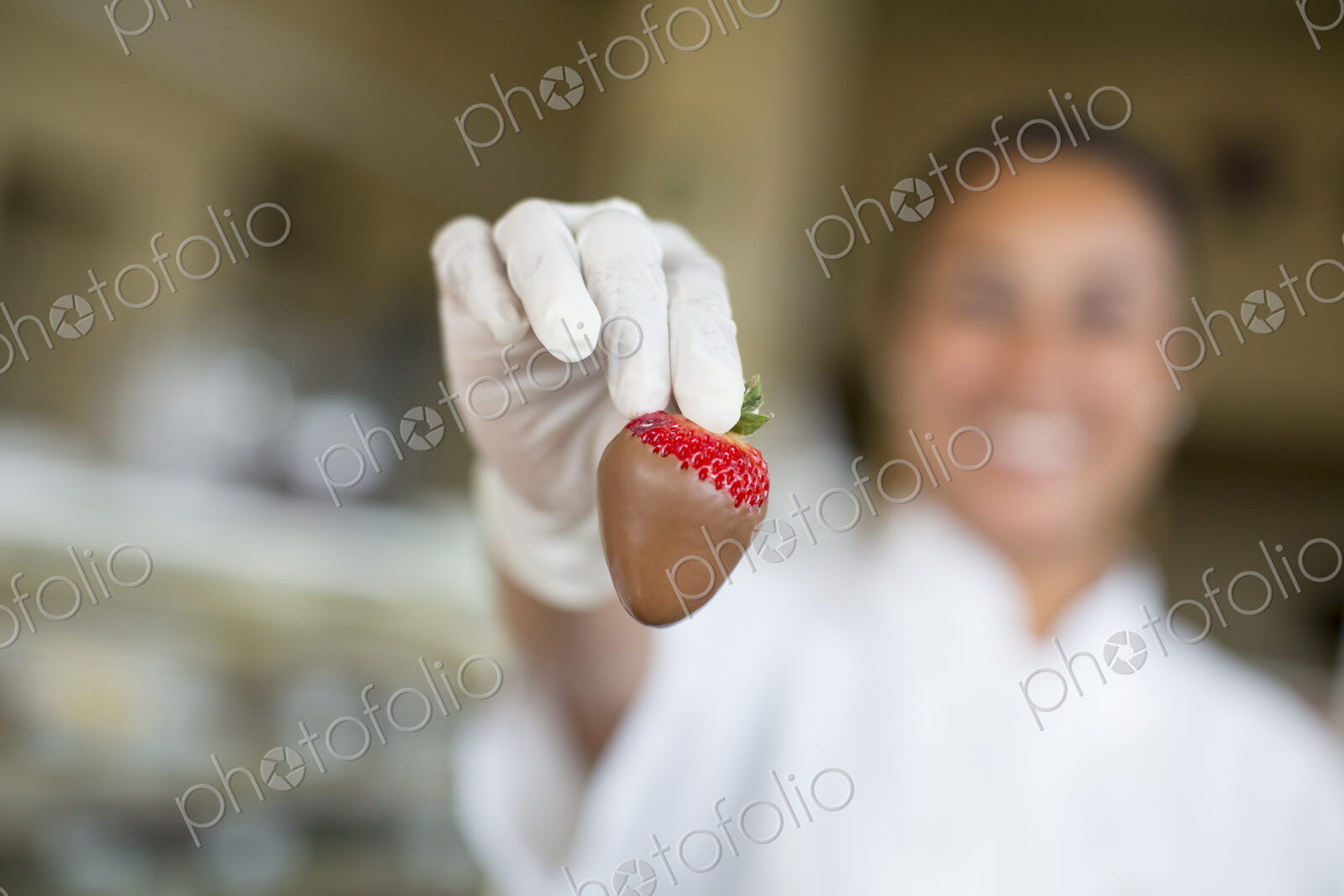 Hispanic woman holding a chocolate covered strawberry in a candy shop.