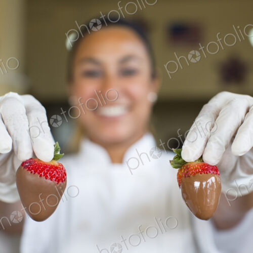 Hispanic woman holding a chocolate covered strawberry in a candy shop. Hispanic woman holding a chocolate covered strawberry in a candy shop.