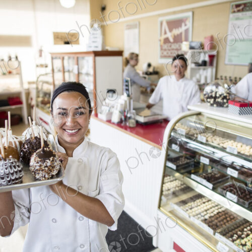 Hispanic woman owner of a candy shop and her staff in the backround of the shop. Hispanic woman owner of a candy shop and her staff in the backround of the shop.