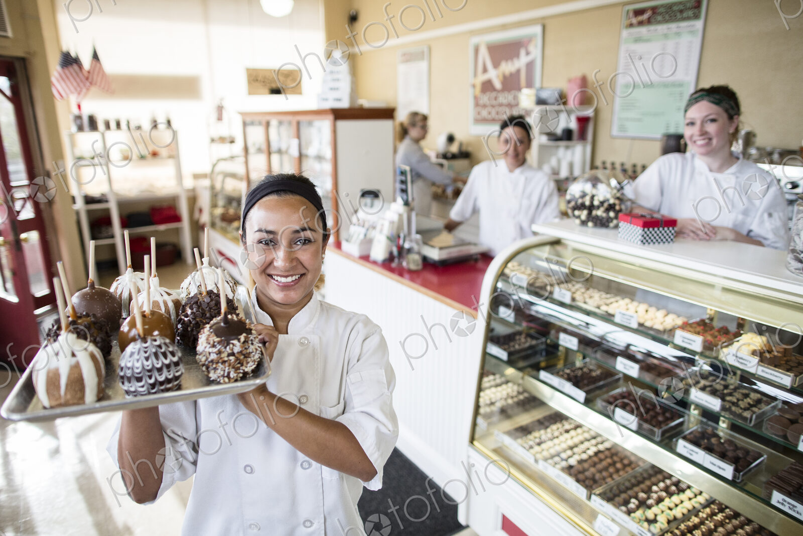 Hispanic woman owner of a candy shop and her staff in the background of the shop.