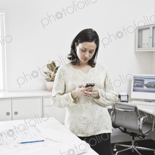 Hispanic woman working on cell phone in an architect's office Hispanic woman working on cell phone in an architect's office