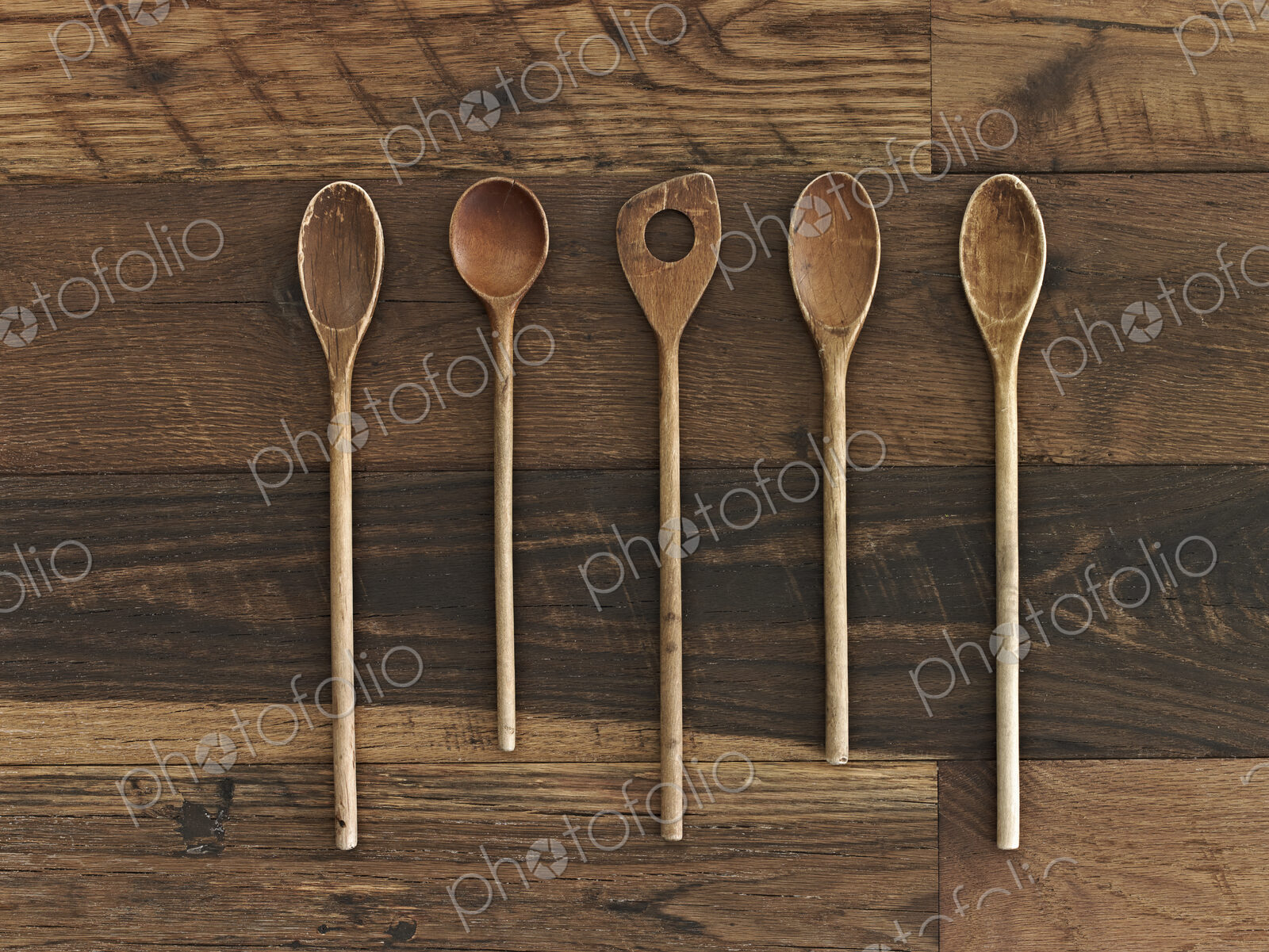Home cooking. A wooden table with a varied wood grain and colour. Five wooden spoons…