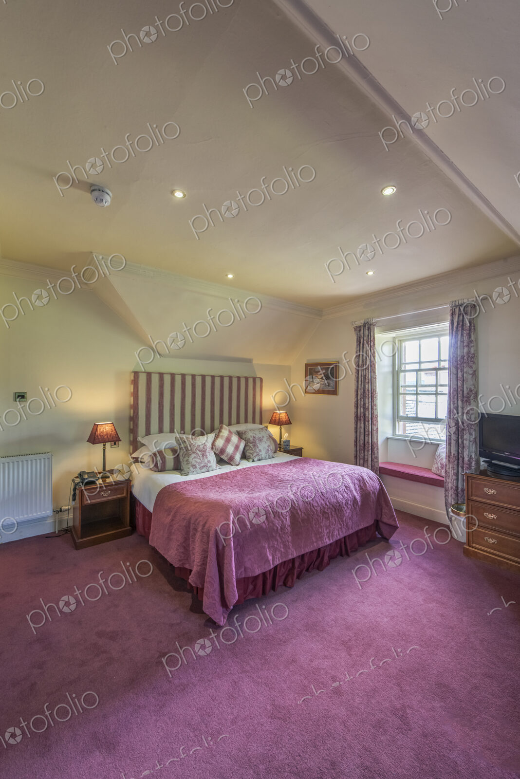 Hotel bedroom with taditional decor and sloped ceiling.