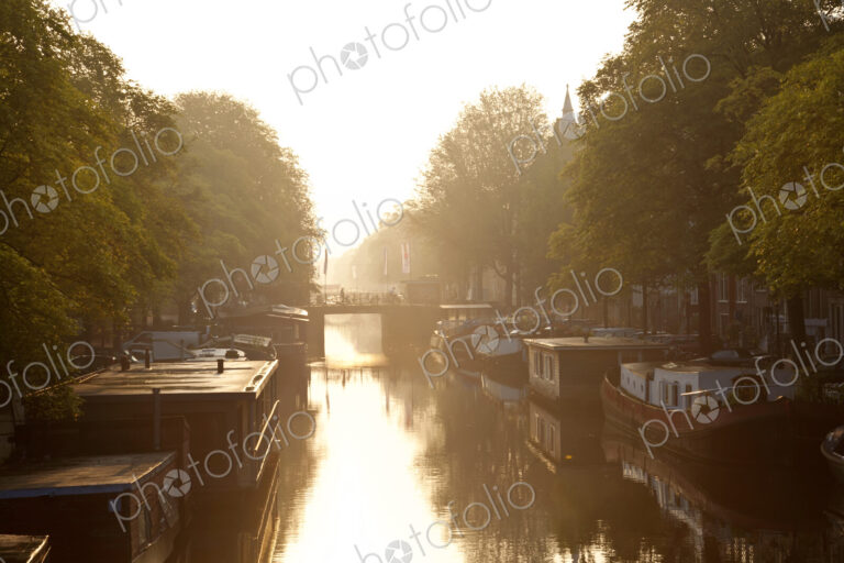 House boats moored on tree-lined canal at sunrise.