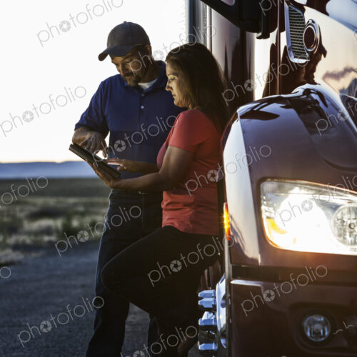 Husband and wife driving team checking their notebook computer log while standing next… Husband and wife driving team checking their notebook computer log while standing next…