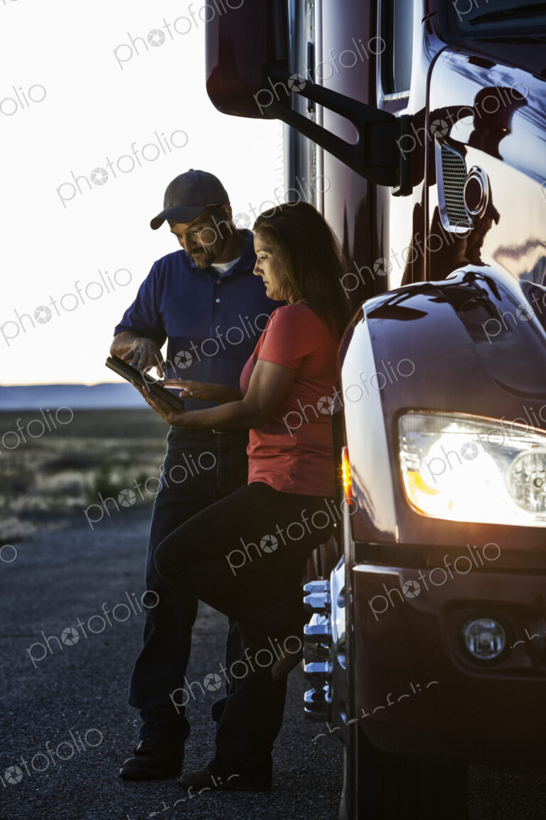 Husband and wife driving team checking their notebook computer log while standing next…