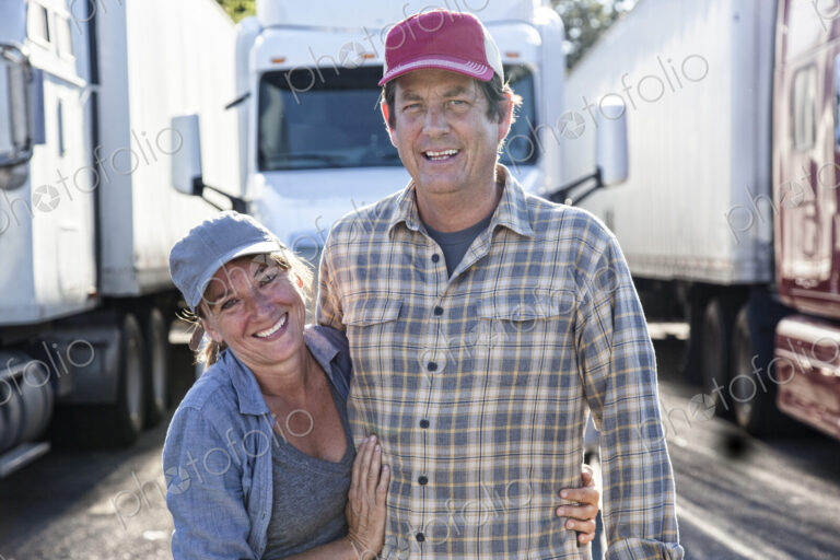 Husband and wife driving team in front of their commercial truck at a truck stop.