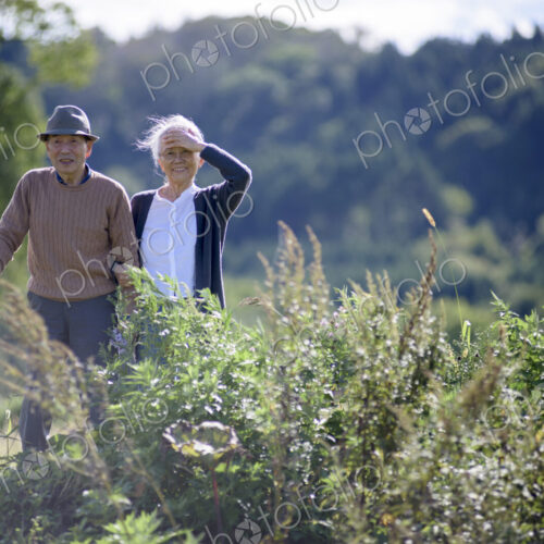 Husband and wife, elderly man wearing hat and using walking stick and elderly woman…