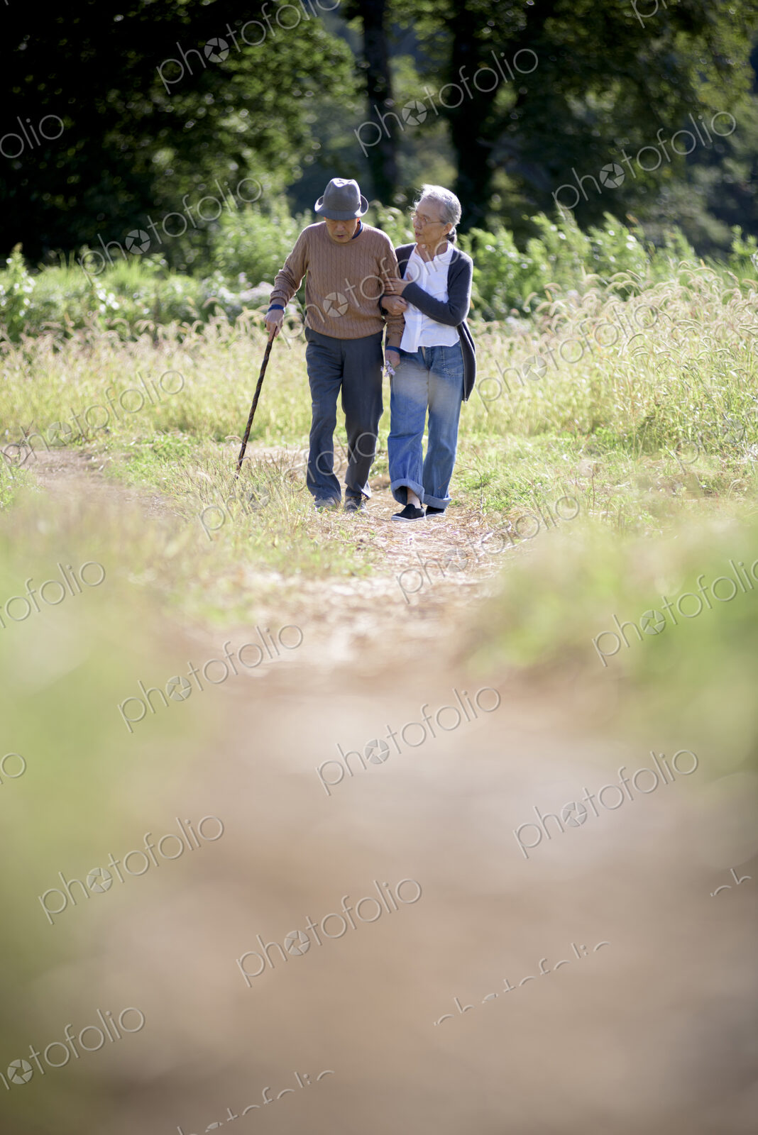 Husband and wife, elderly man wearing hat and using walking stick and elderly woman…