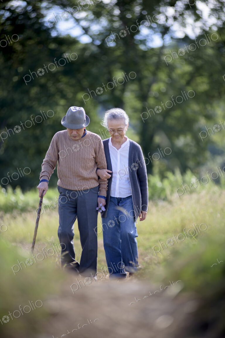Husband and wife, elderly man wearing hat and using walking stick and elderly woman…