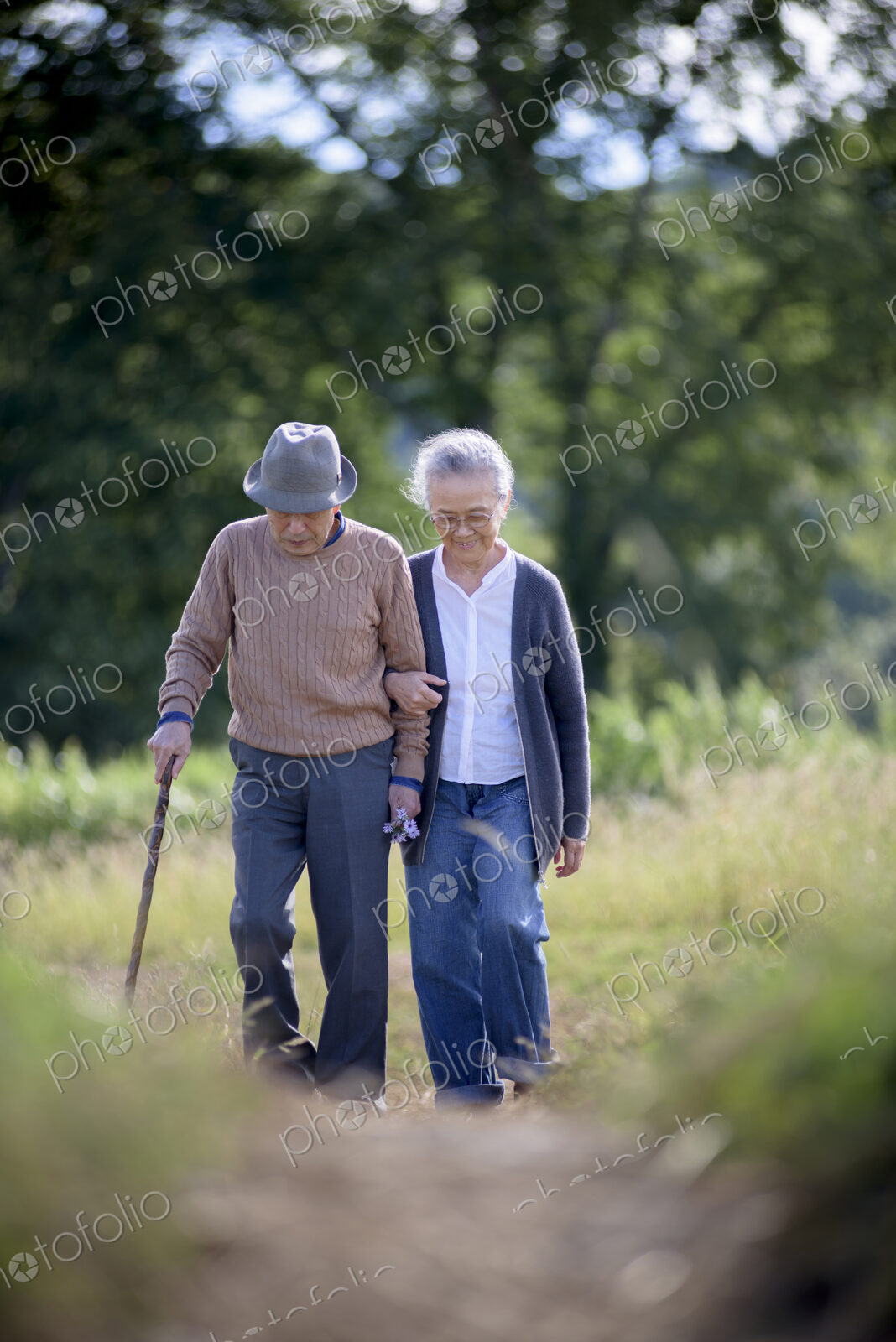 Husband and wife, elderly man wearing hat and using walking stick and elderly woman…