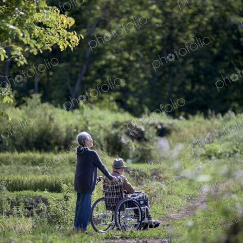 Husband and wife, elderly woman pushing elderly man wearing hat in a wheelchair. Husband and wife, elderly woman pushing elderly man wearing hat in a wheelchair.