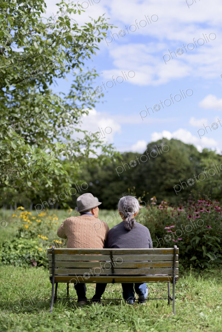 Husband and wife, rear view of elderly man wearing hat and woman sitting side by side…
