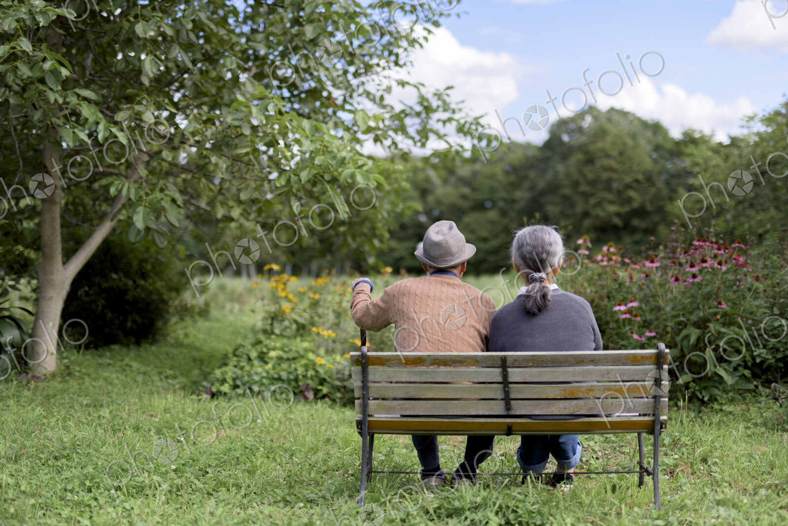Husband and wife, rear view of elderly man wearing hat and woman sitting side by side…