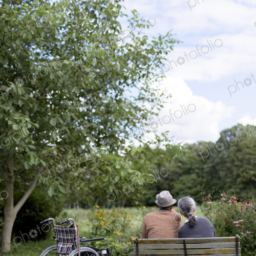 Husband and wife, rear view of elderly man wearing hat and woman sitting side by side…