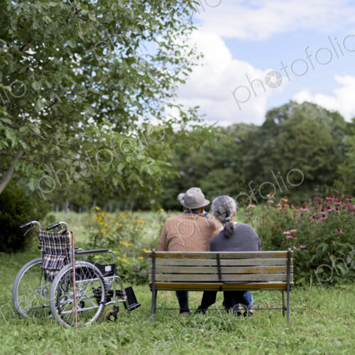 Husband and wife, rear view of elderly man wearing hat and woman sitting side by side…