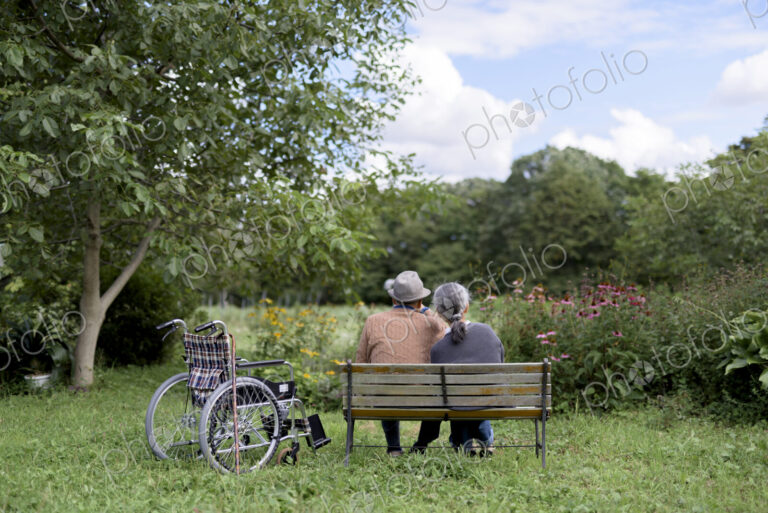 Husband and wife, rear view of elderly man wearing hat and woman sitting side by side…
