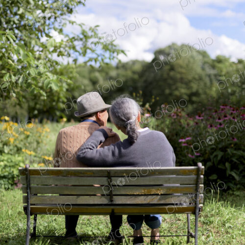Husband and wife, rear view of elderly man wearing hat and woman sitting side by side…