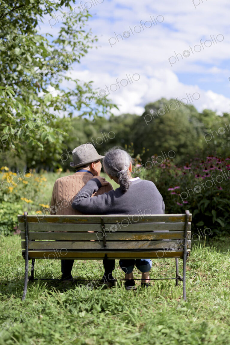 Husband and wife, rear view of elderly man wearing hat and woman sitting side by side…